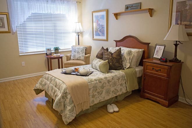 A cozy and well-decorated bedroom with a bed, nightstand, chair, and window.