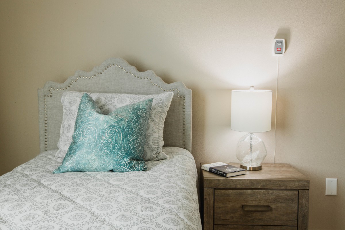 A cozy bedroom with a neatly made bed, featuring a fluffy turquoise pillow and a stylish lamp on the nightstand.