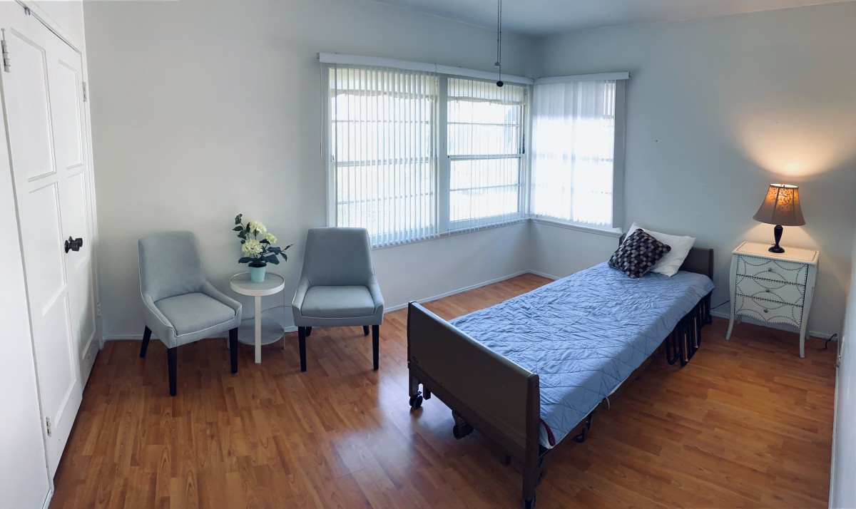 A minimalist bedroom with a single bed and chairs, filled with natural light from large windows.