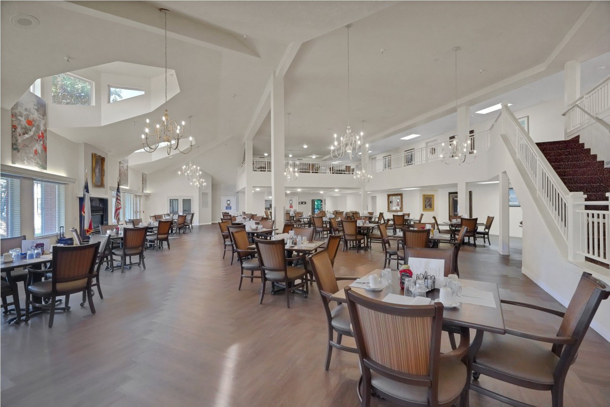 A spacious and bright dining room with neatly arranged tables and chairs, illuminated by elegant chandeliers.