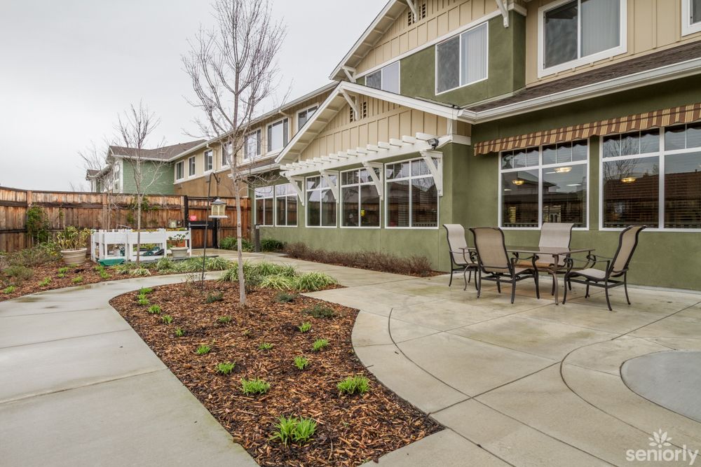 A well-maintained garden area with a paved pathway and patio furniture, adjacent to a two-story building.