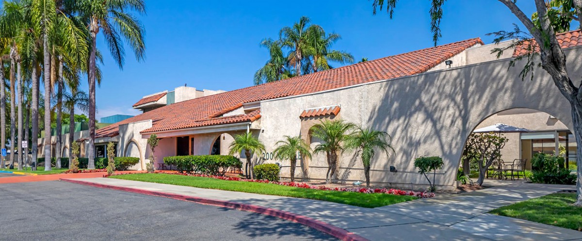 A suburban house with a red-tiled roof and palm trees in front, under a clear blue sky.
