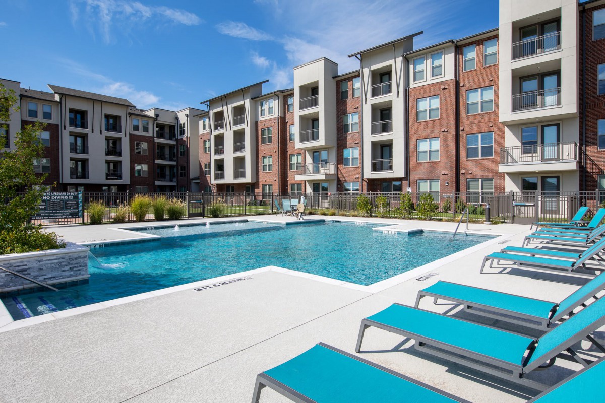 Modern apartment complex with an outdoor swimming pool and lounging area.