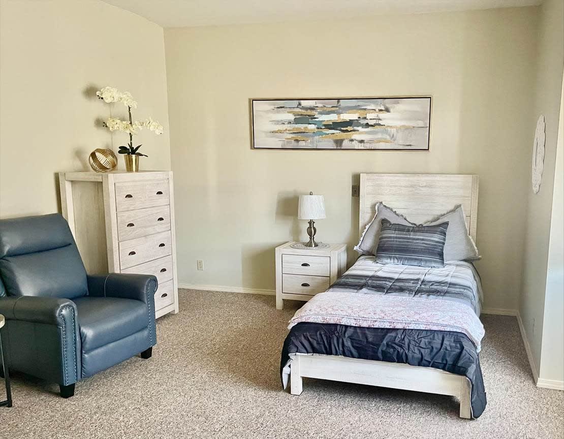 A cozy bedroom with a single bed, armchair, and dresser, complemented by wall art and decor.