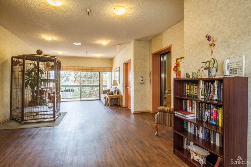 A cozy hallway with a wooden floor, bookshelves, and a seating area by the window.
