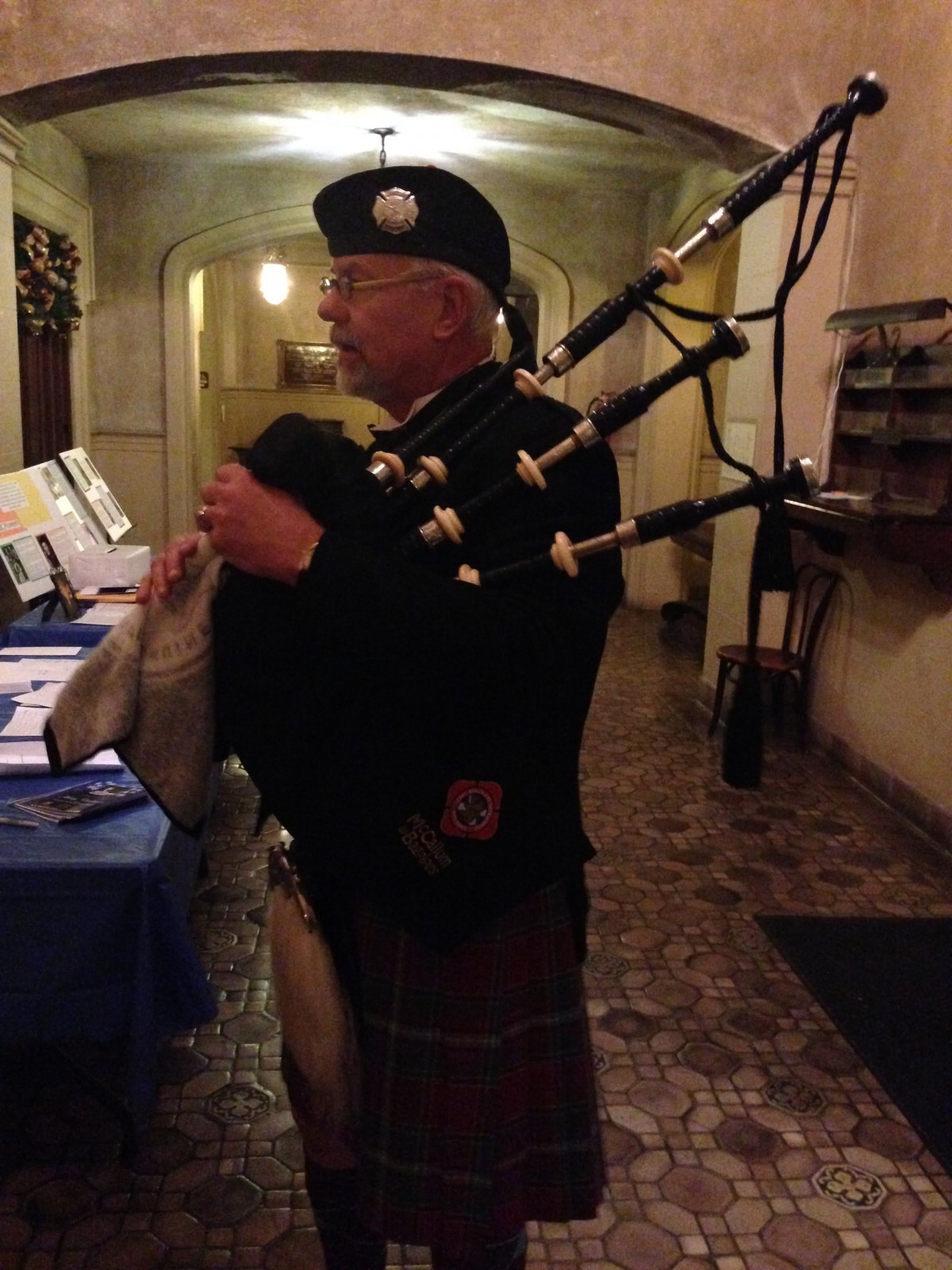 A bagpiper dressed in traditional Scottish attire playing indoors.
