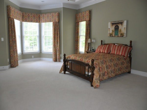 A spacious bedroom with a wooden bed, large windows, and elegant curtains.