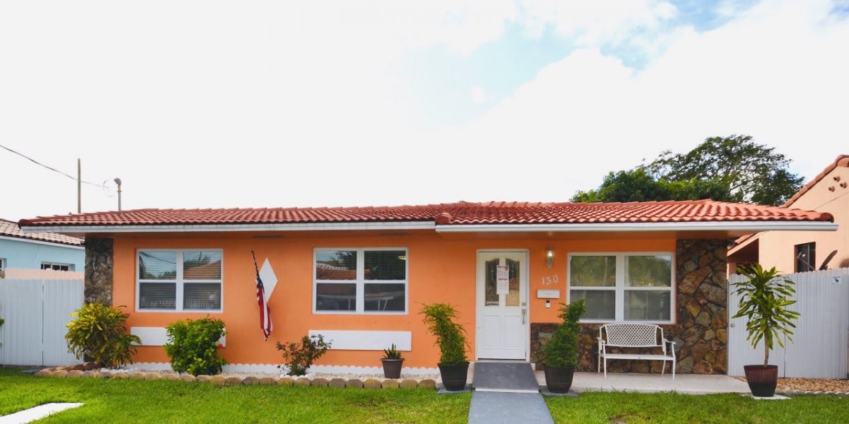 A small orange house with a well-kept lawn and potted plants in front.