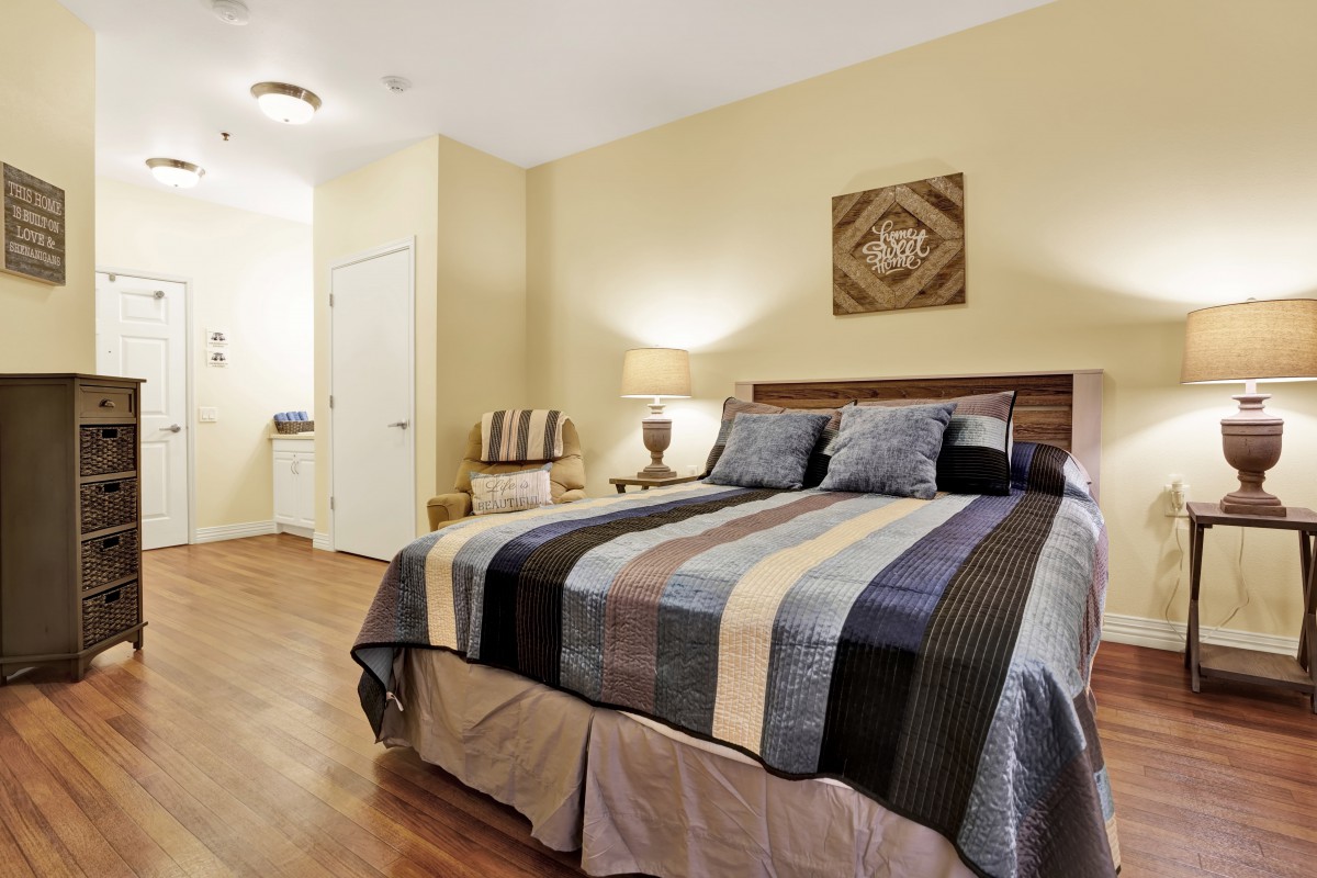 A cozy bedroom with a striped bedspread, wooden flooring, and warm lighting.
