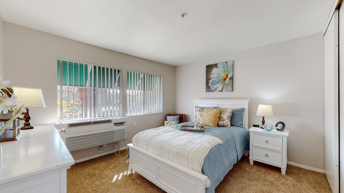 A cozy bedroom with a neatly made bed, nightstands, and large windows allowing natural light.