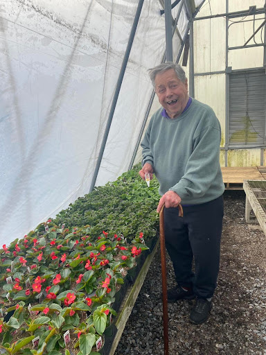 An elderly man joyfully tending to plants in a greenhouse.