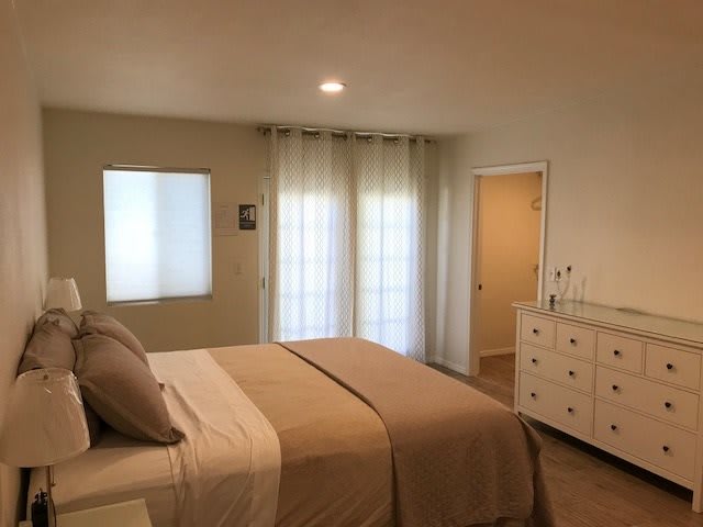 A cozy bedroom with a neatly made bed and soft lighting, featuring neutral tones and simple decor.