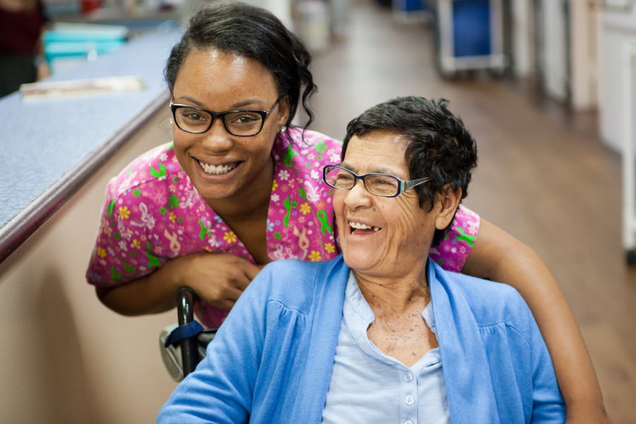 A healthcare worker smiling with an elderly patient in a wheelchair.