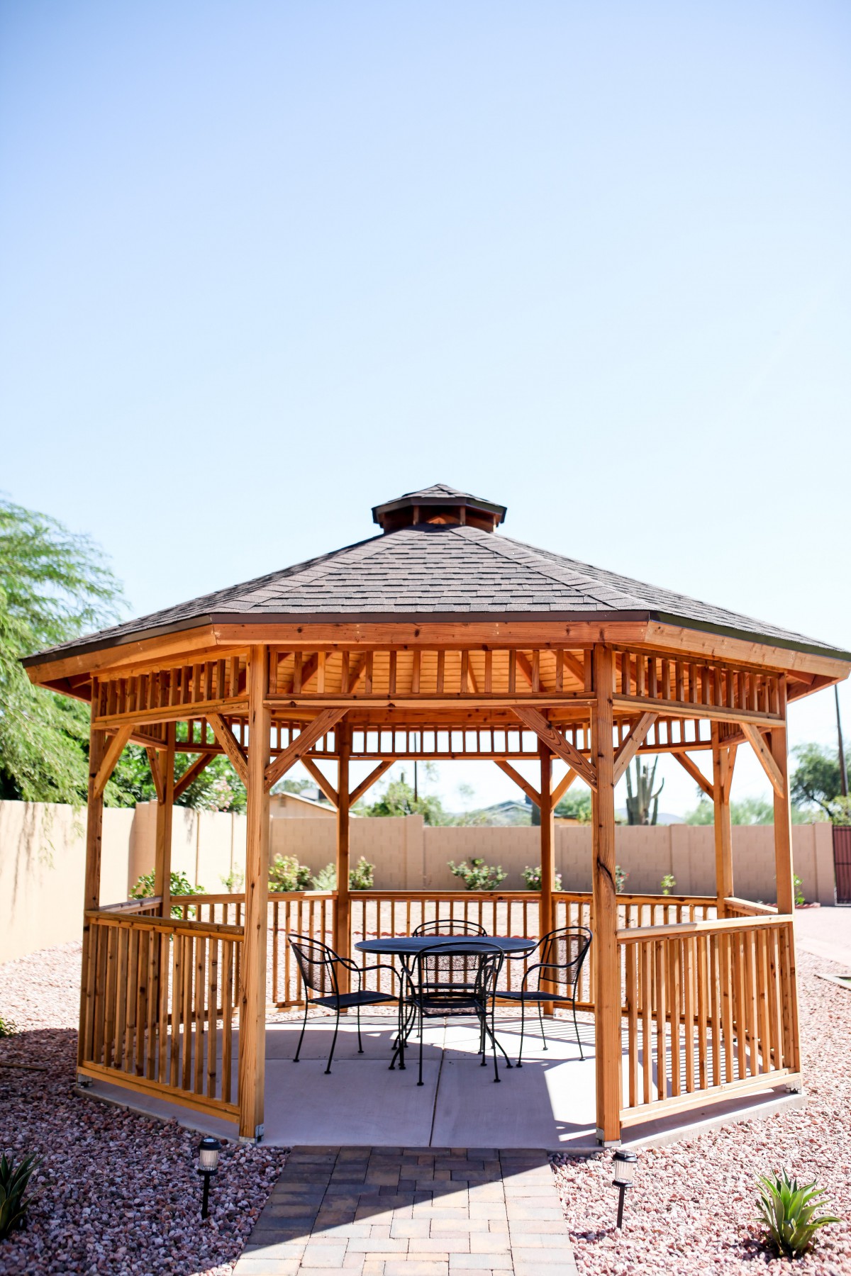 A wooden gazebo in a sunny backyard setting.