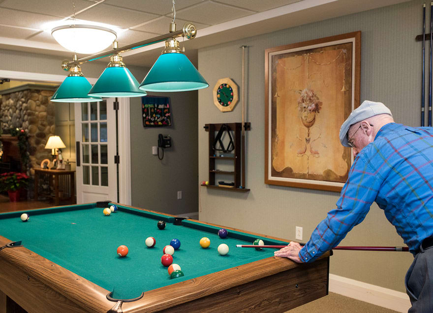 A man wearing a hat stands by a pool table in a recreation room.
