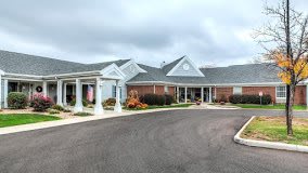 An exterior view of a building with a driveway and landscaped entrance under a cloudy sky.