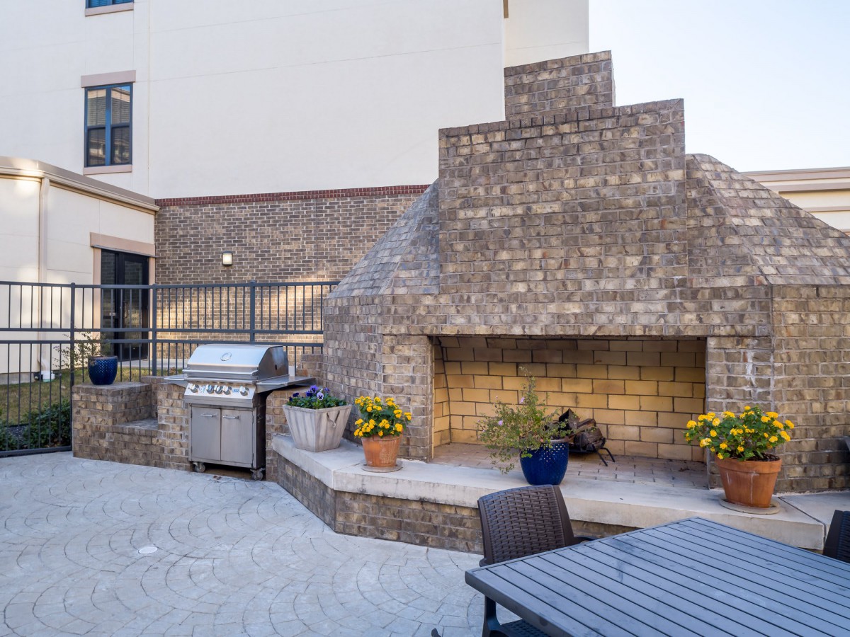 An outdoor patio features a large stone fireplace, a barbecue grill, and seating with potted plants for decoration.