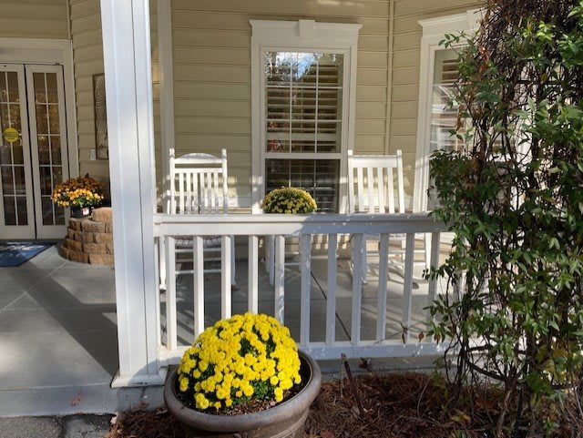 A cozy porch with white rocking chairs and vibrant potted flowers.