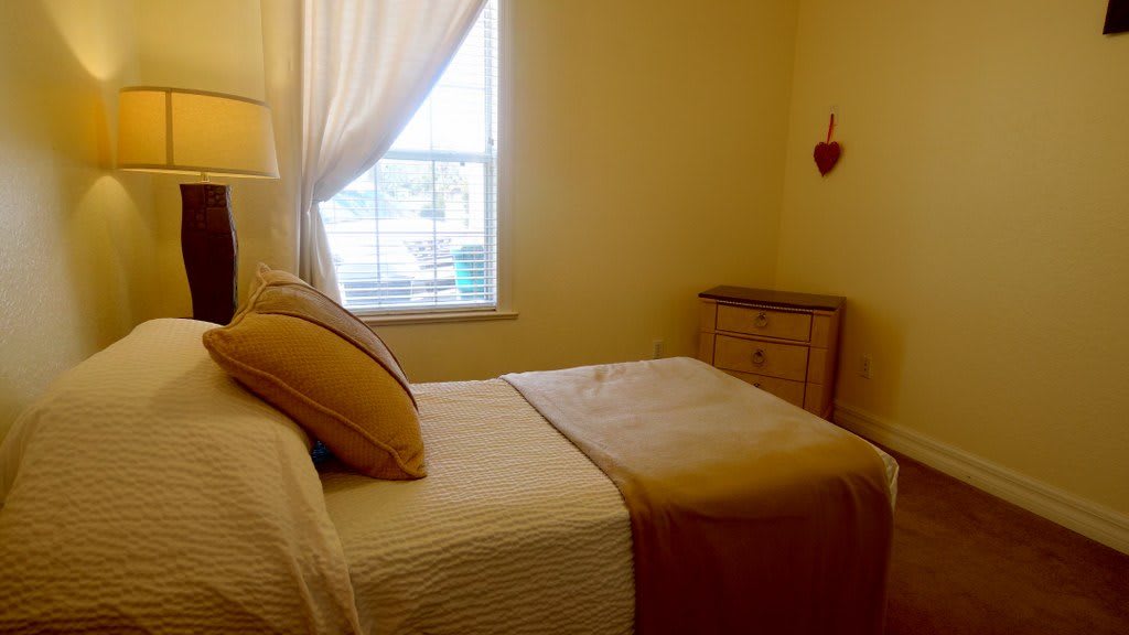 A cozy bedroom with a neatly made bed, soft lighting, and a window with curtains.