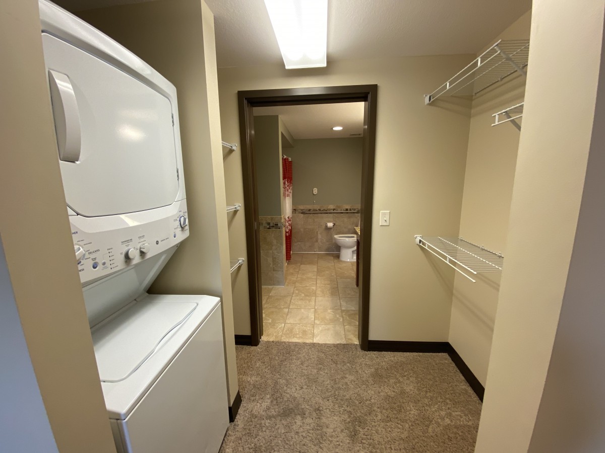 A laundry room featuring stacked washer and dryer units, adjacent to a walk-in closet.