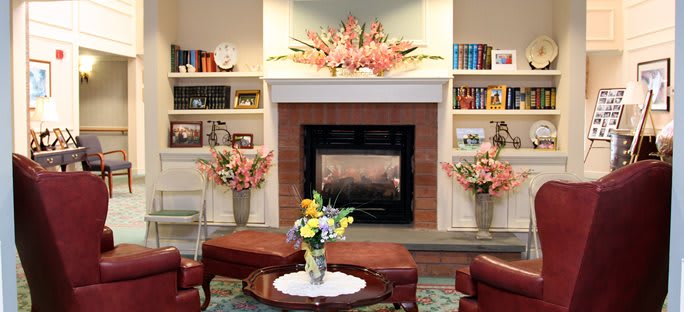 A cozy living room with a central fireplace, adorned with floral arrangements and surrounded by bookshelves.