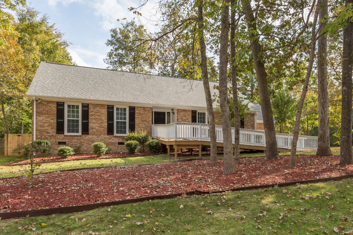 A brick ranch-style house surrounded by trees and landscaped front yard.
