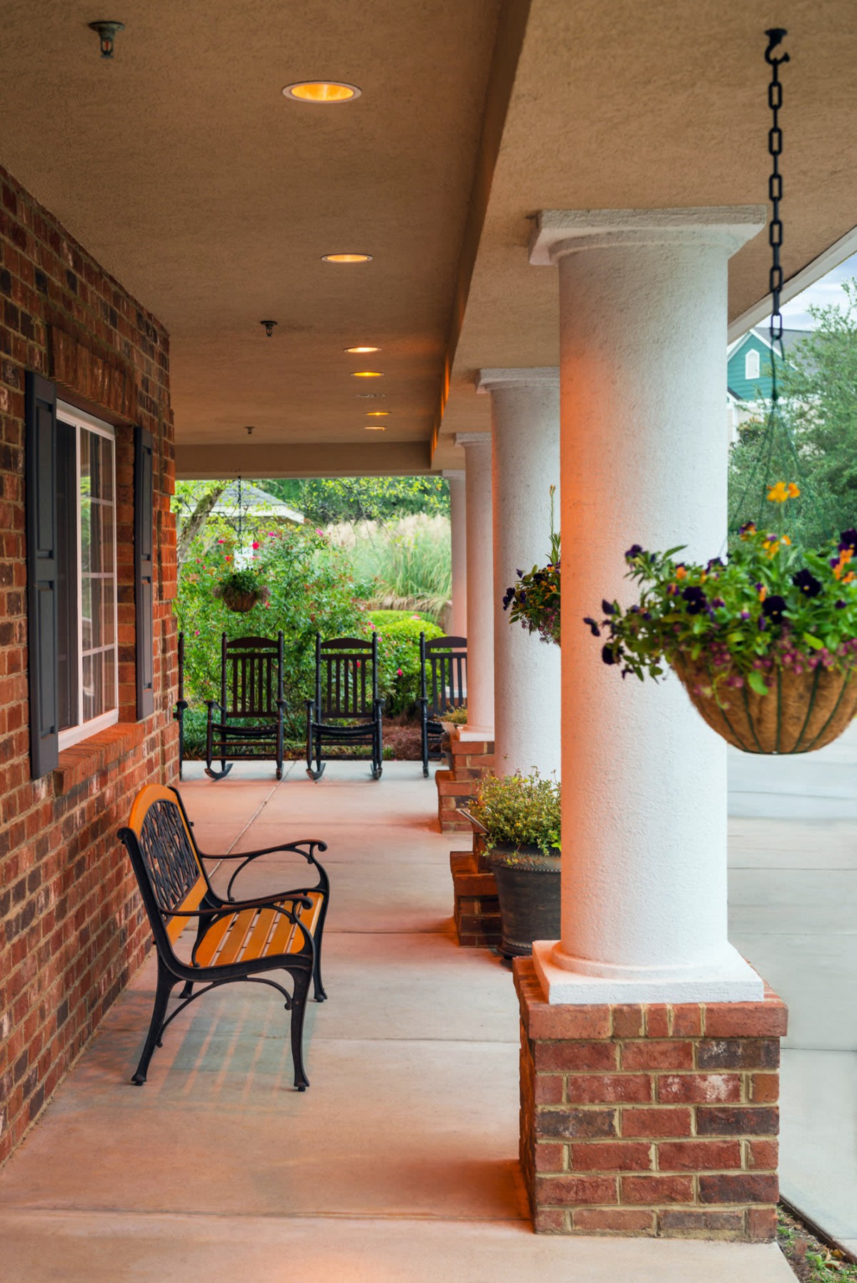 A cozy porch area with a bench, surrounded by hanging plants and framed by white columns.