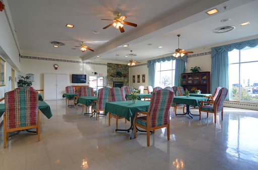 A spacious and brightly lit dining area designed for community gatherings, featuring tables covered with green cloth and comfortable seating.