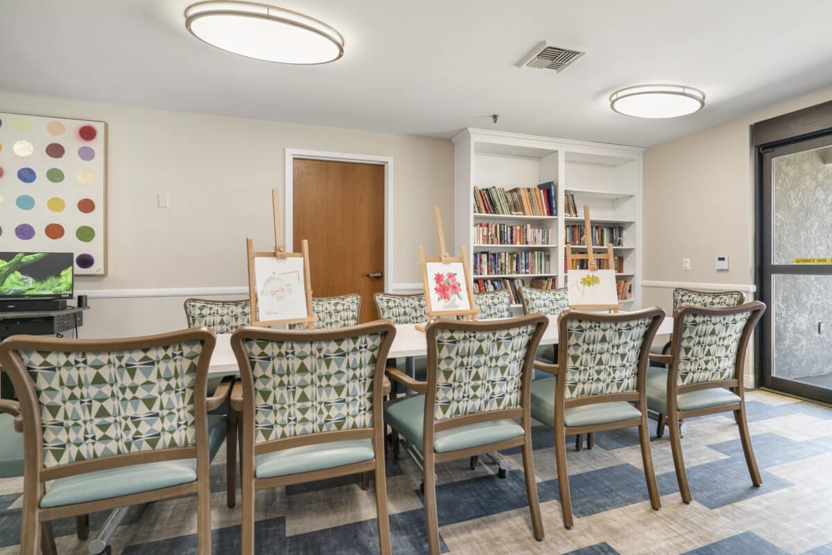 A well-appointed library meeting room featuring a row of chairs, bookshelves, and art easels.
