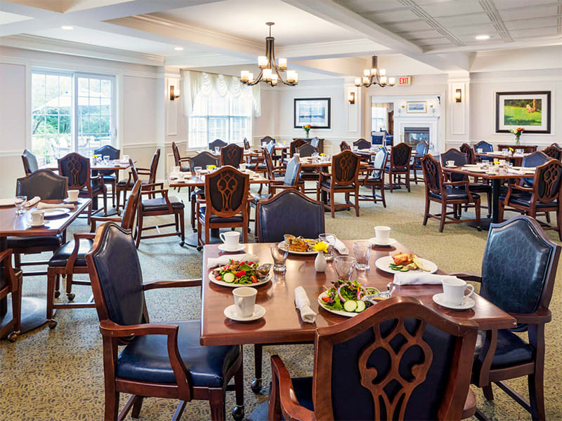 An elegant dining room setting with multiple tables prepared for guests, featuring neatly arranged chairs and plates of food.