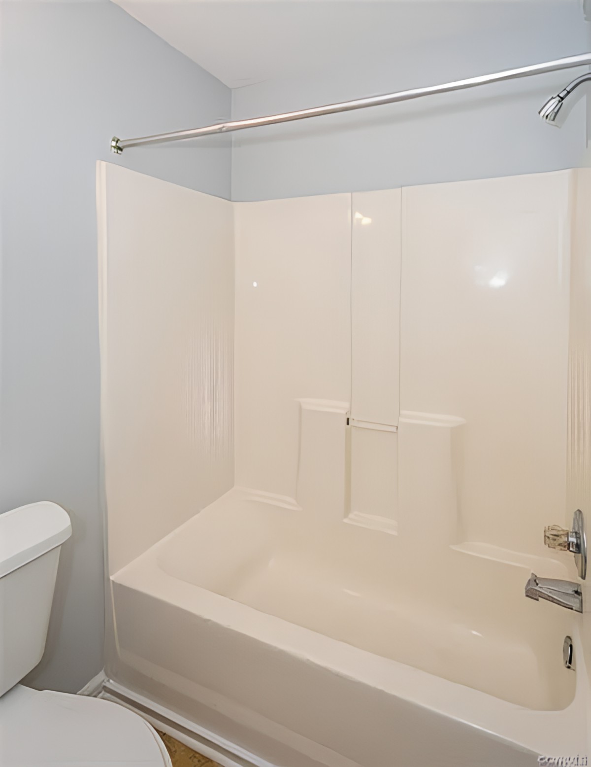 A clean and simple bathroom featuring a white bathtub with an integrated shower, alongside a toilet.