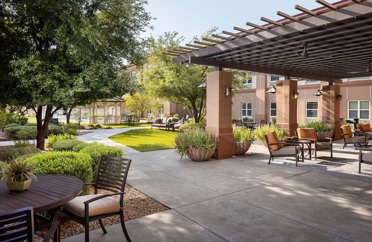 A serene garden with outdoor seating under a pergola, surrounded by lush greenery.