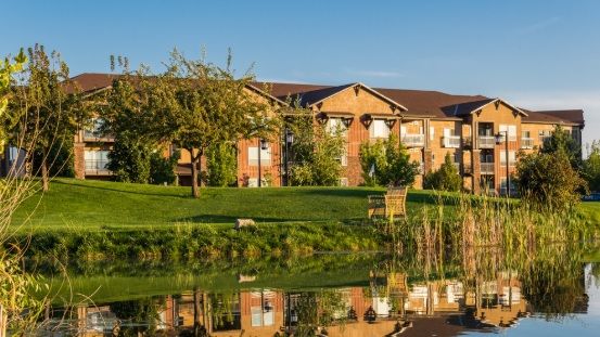 A scenic view of a building reflected in a lake surrounded by trees and grass.