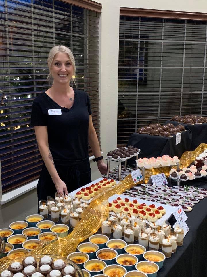 A person standing behind a table filled with various desserts and pastries at an event.