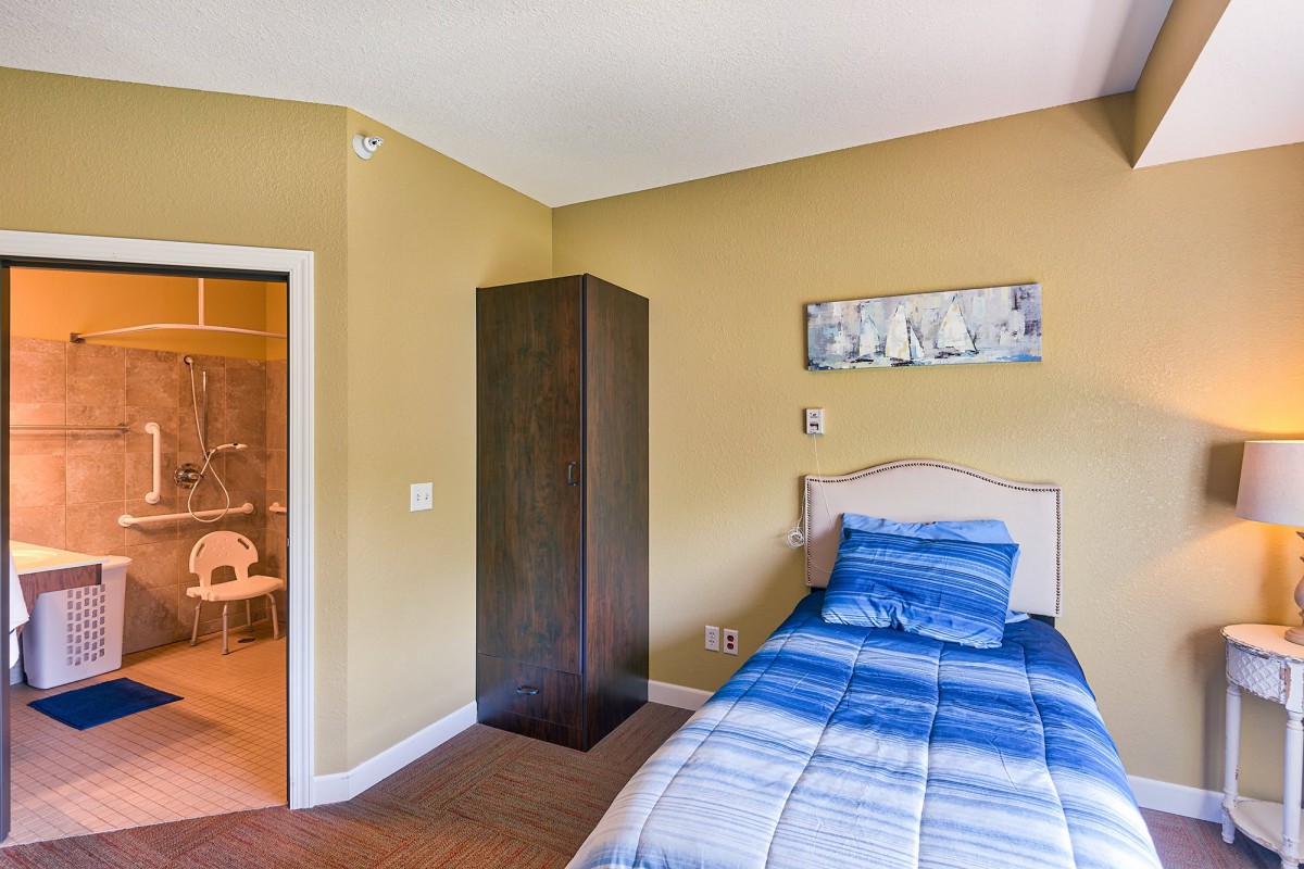 A simple bedroom featuring a single bed with blue bedding, a dark wardrobe, and minimalist decor.