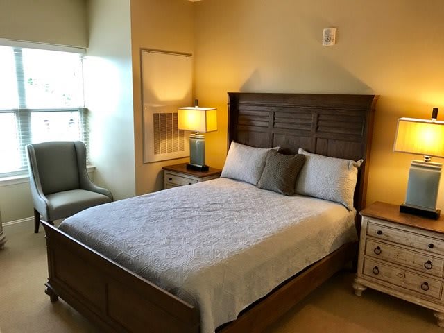 A cozy bedroom with a neatly made bed, wooden headboard, and bedside lamp.