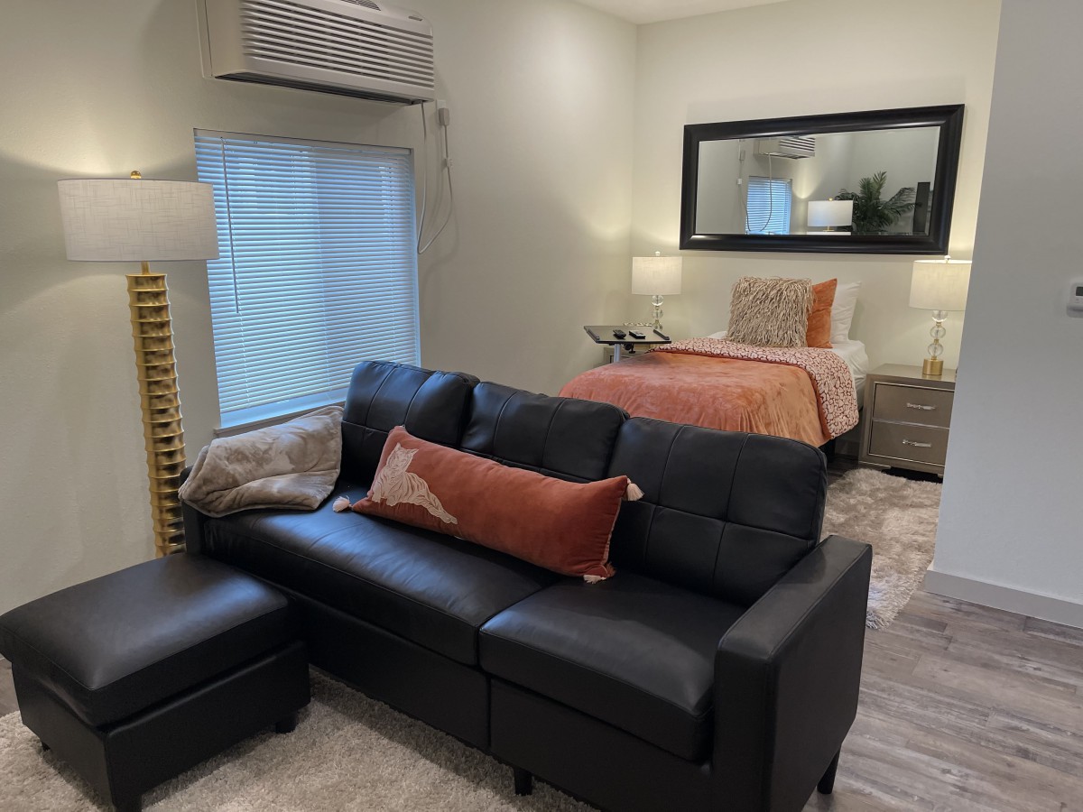 A modern studio apartment featuring a cozy living area with a black sofa and an adjacent bedroom space.