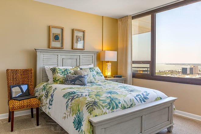 A cozy bedroom with floral bedding and large windows offering a view.