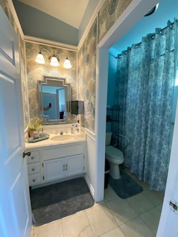 A cozy bathroom featuring a vanity with a mirror, decorative lighting, and a patterned shower curtain.