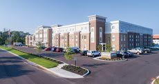 A modern hotel building with a brick exterior, surrounded by a parking lot and landscaped grounds.