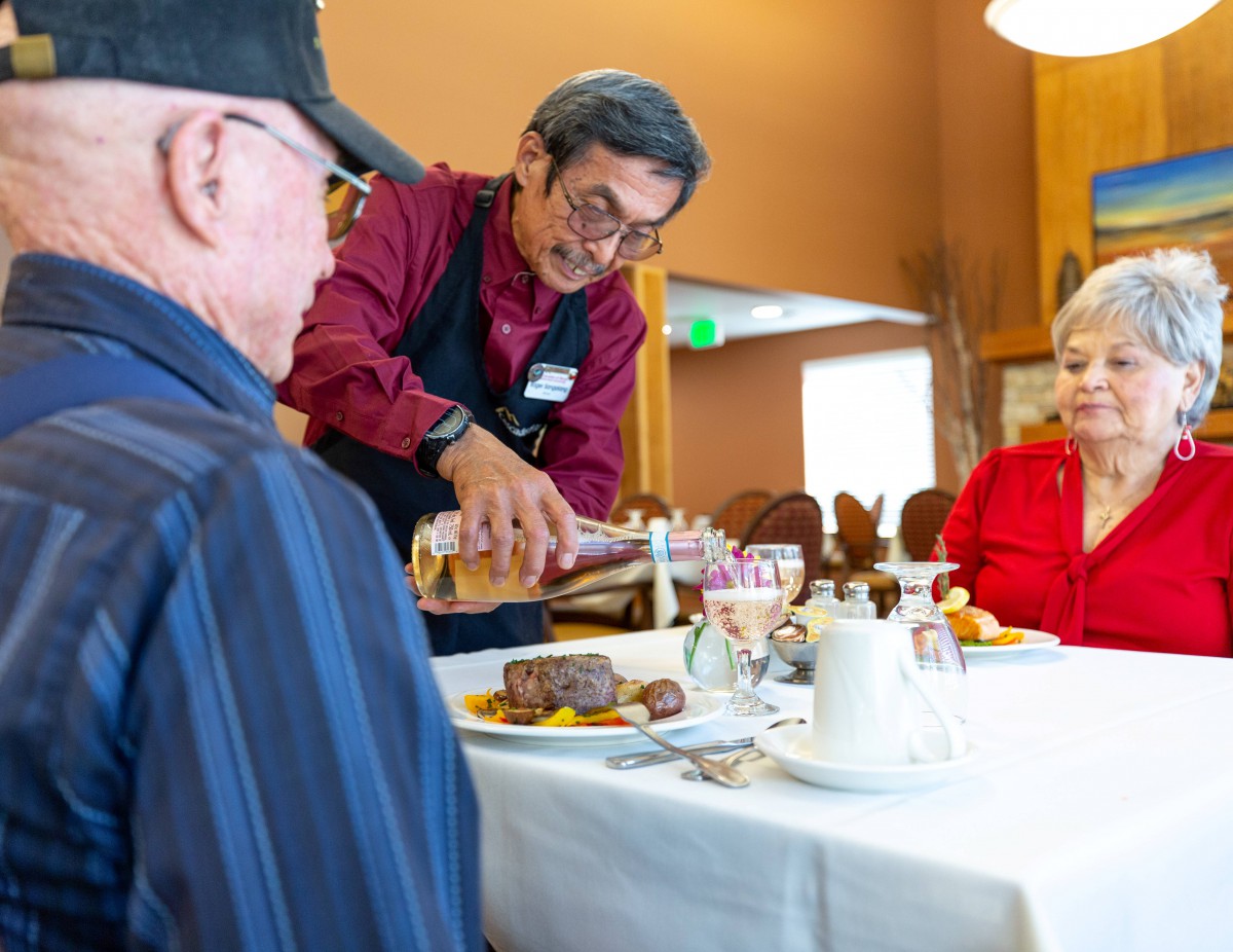 A waiter serving food to diners at a restaurant table.
