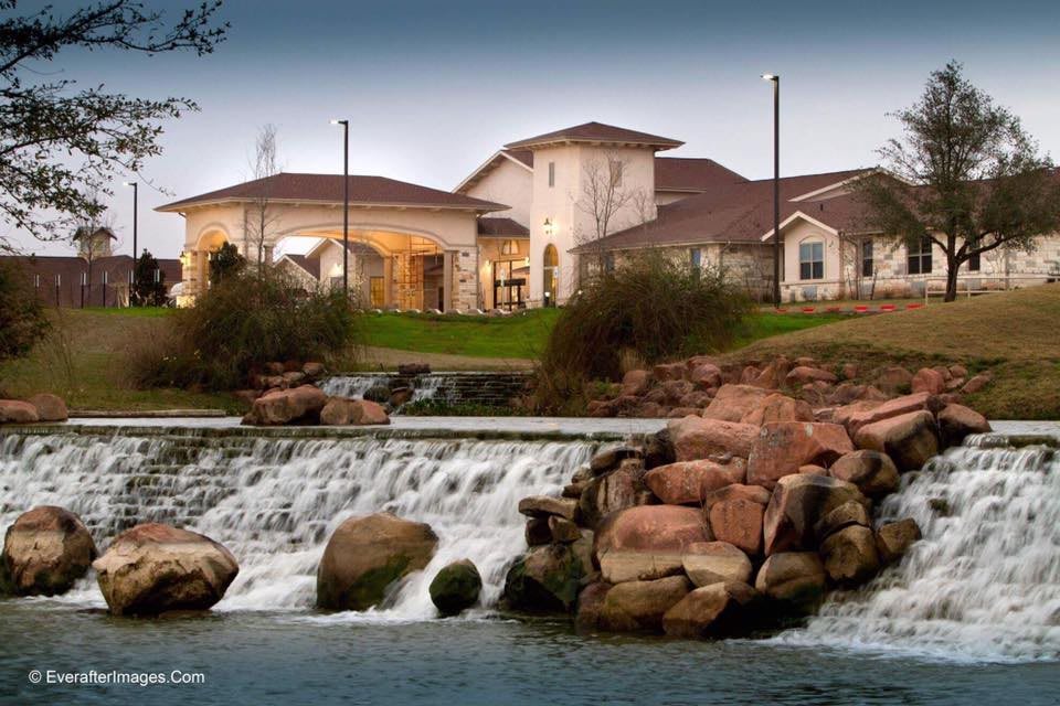 A scenic view of a building situated behind a waterfall and rocky landscape.