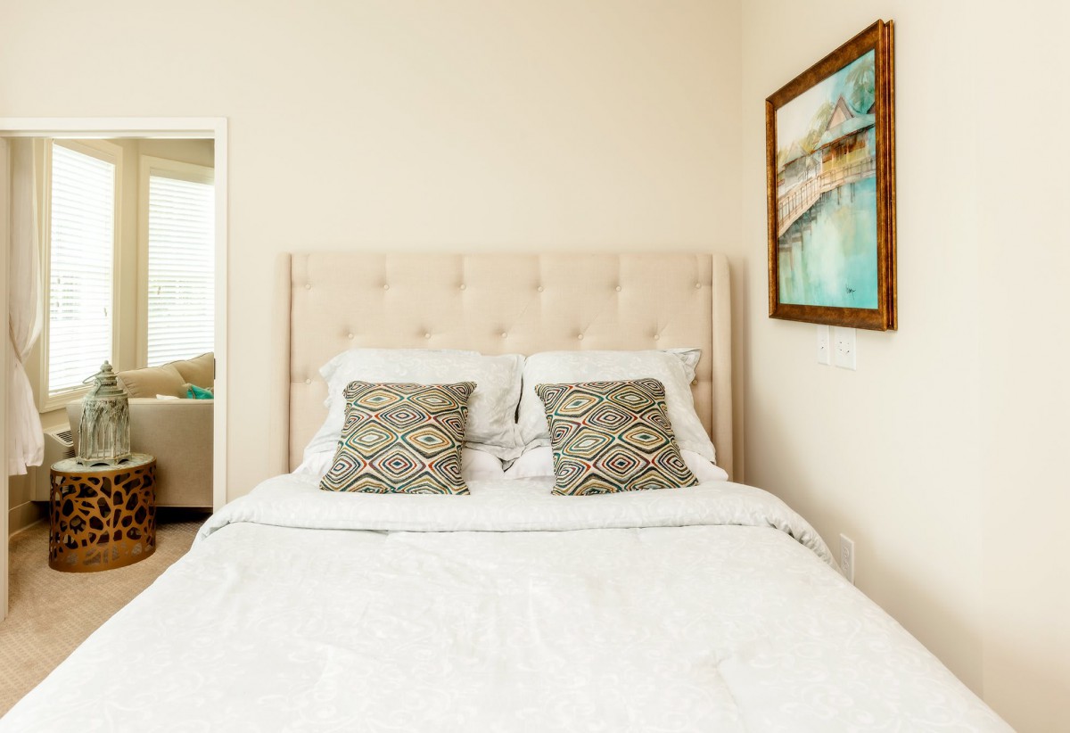 A neatly made bed with patterned pillows and a framed artwork on the wall in a cozy bedroom.