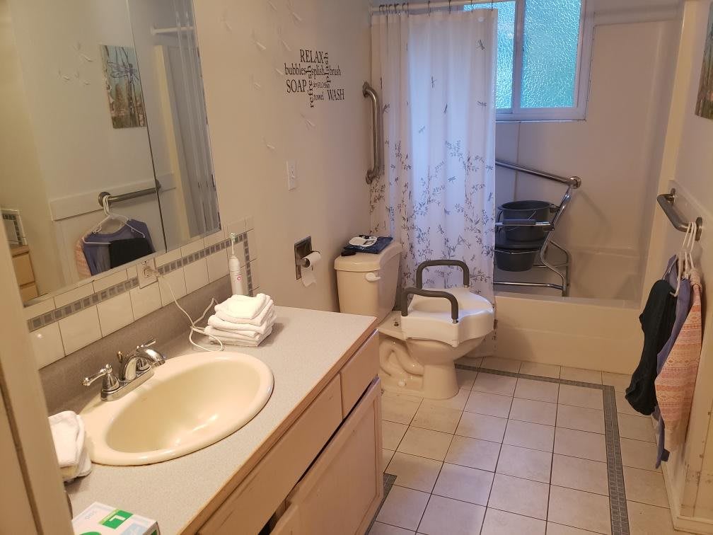 A bathroom with a sink, toilet, and shower area featuring accessibility aids.