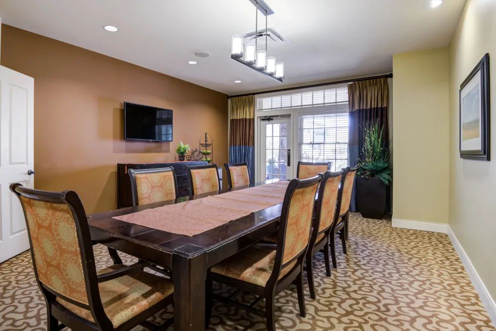 A well-furnished dining or conference room featuring a long table surrounded by chairs, with modern lighting and decor.