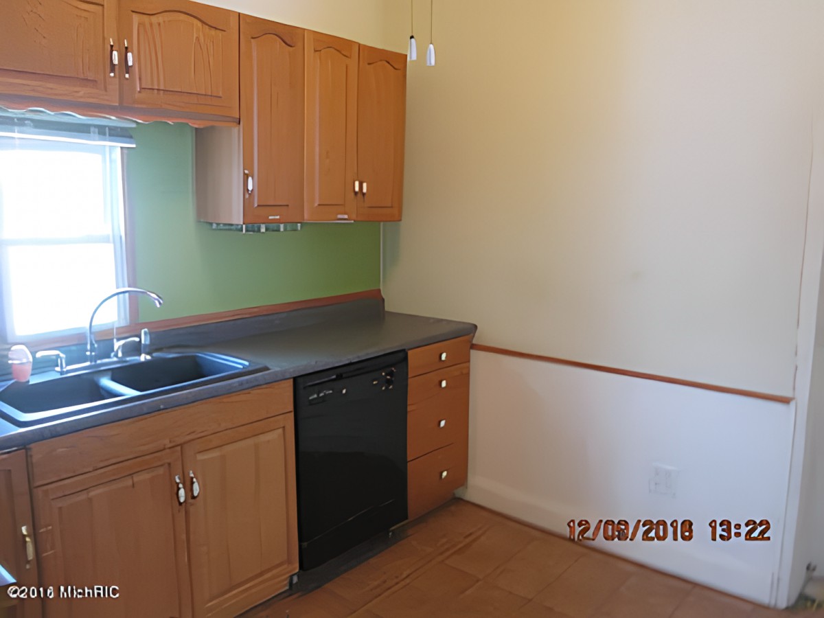 An empty kitchen with wooden cabinets, a sink, and a dishwasher.