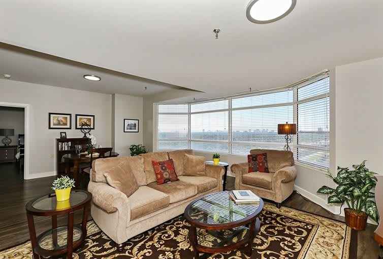 A cozy living room with a large sofa, armchair, and coffee table, featuring decorative elements and a view through the windows.
