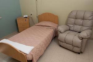 A simple room with a bed, a nightstand, and a reclining chair.