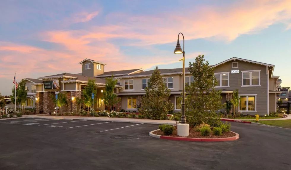 A residential building with trees and a parking lot under a colorful sunset sky.