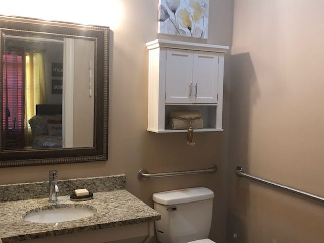 A modern bathroom with a granite countertop, mirror, cabinet, and toilet.